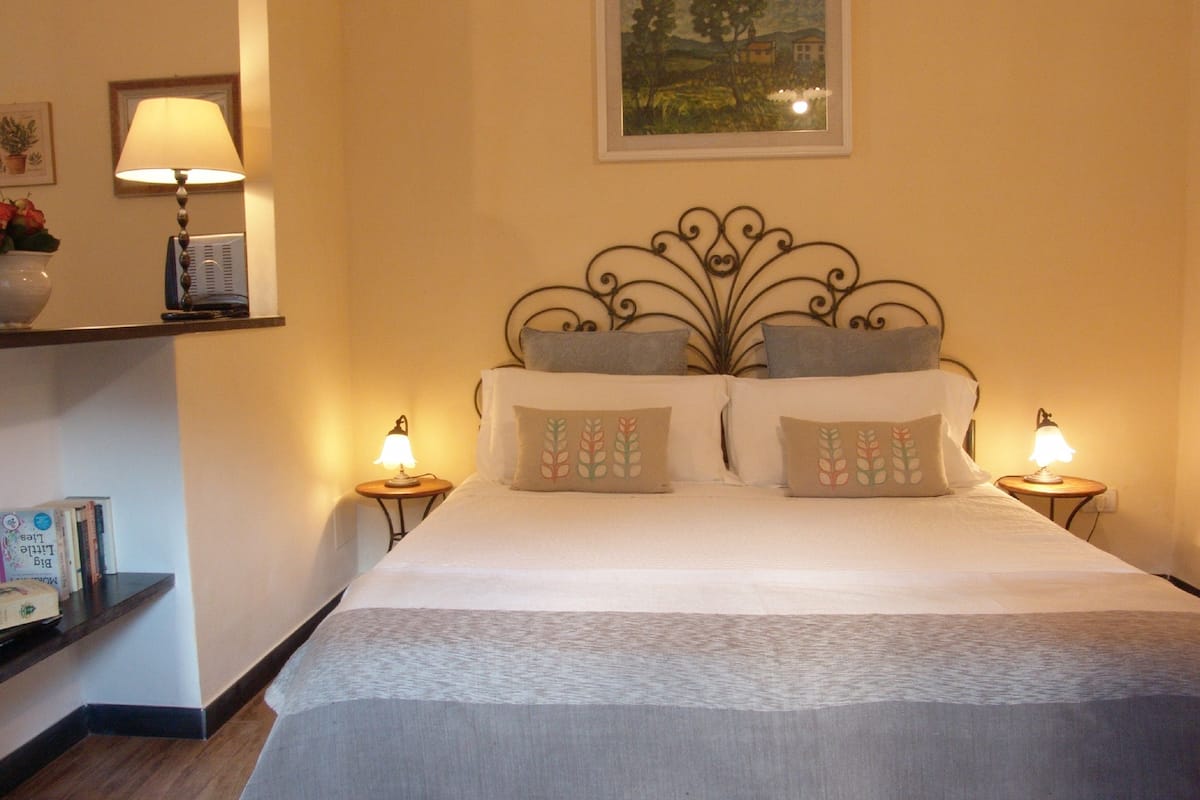 A neatly made bed with a decorative headboard, two bedside lamps, and a framed landscape painting on the wall.