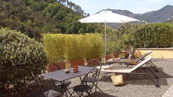 An outdoor patio with a table and chairs, a sun umbrella, and lounge chairs.
