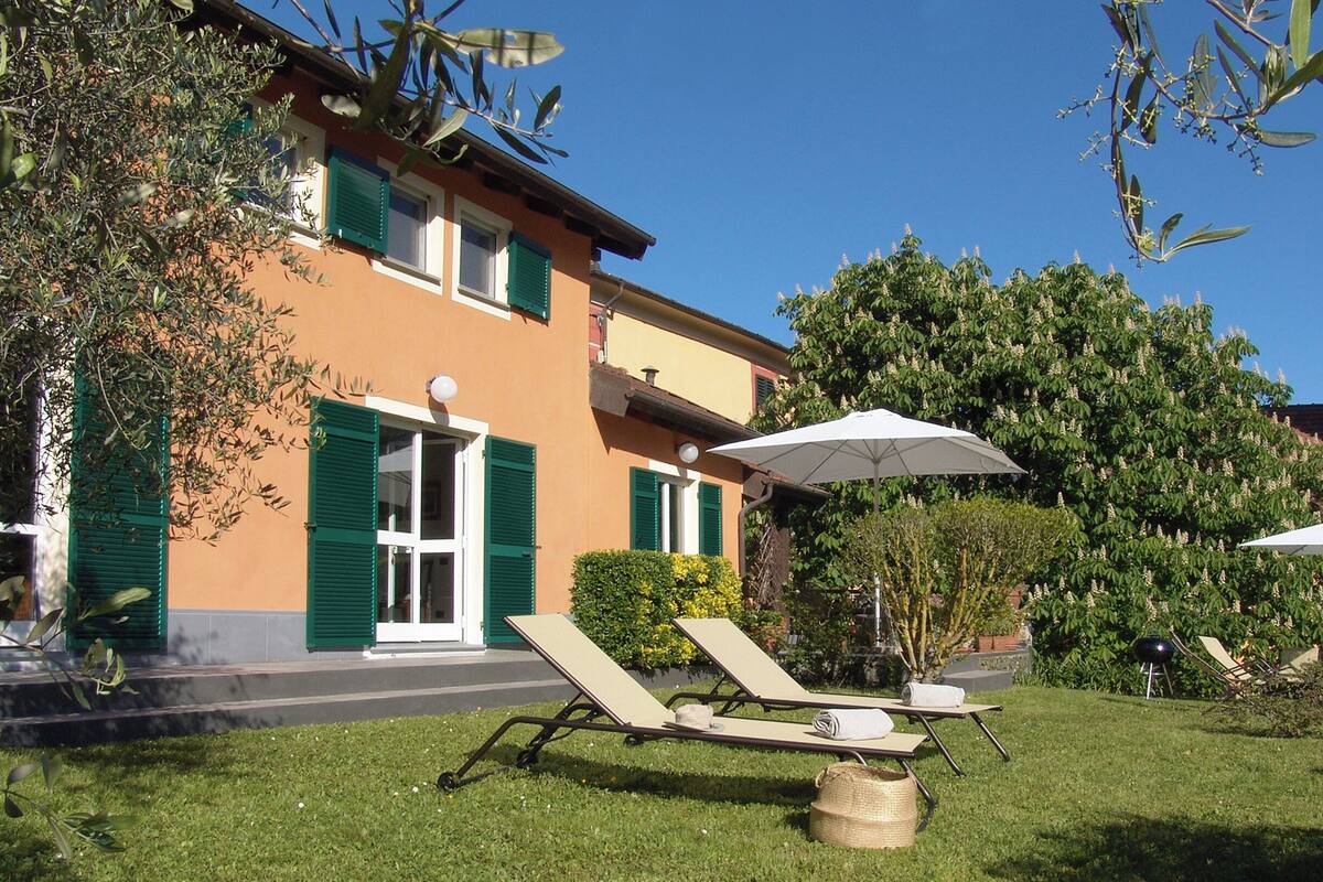 A building with a tower, a lawn with sun loungers, and a white umbrella.