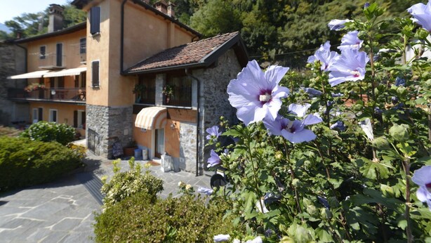 A building with a stone facade, a tiled roof, and a balcony with potted plants. - Casa Rosalba - WelcHome (Cannobio)