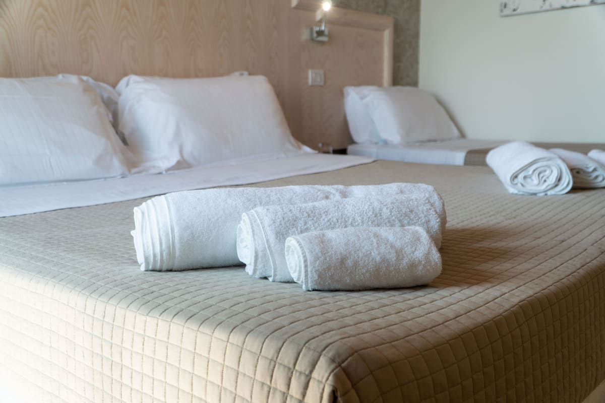 Un lit bien fait, avec une tête de lit matelassée, deux serviettes enroulées et une couverture pliée posée sur un couvre-lit beige.