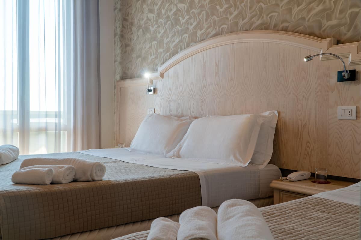 Une chambre d’hôtel avec un grand lit, deux tables de chevet et une petite table de nuit avec une lampe.