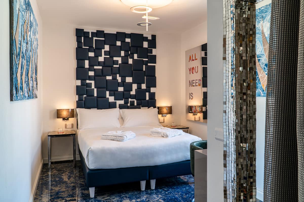 Une chambre d’hôtel moderne avec une tête de lit à motifs géométriques, un lit parfaitement fait, deux lampes de chevet et un élément décoratif mural.