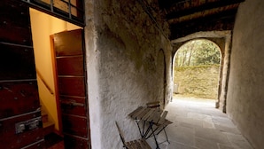 Una habitación rústica con un banco de madera, una pared de piedra y vistas por un ventanal arqueado.