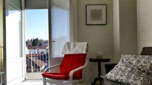 Una habitación con una silla roja, un sofá gris, una mesita y una obra de arte enmarcada en la pared.