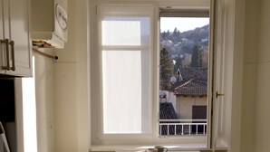 Una cocina con ventana, armarios blancos, una mesita y vistas a edificios.