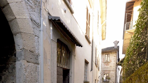 Un estrecho callejón adoquinado flanqueado por edificios de piedra, una puerta pequeña y una reja de metal.