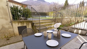 Ein Essbereich im Freien mit einem Tisch für vier Personen, umgeben von Stühlen, einer Blumenvase und Blick auf einen Berg im Hintergrund.