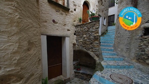 Una estrecha escalera de piedra que sube a una puerta, con una pequeña ventana y plantas en macetas en la parte superior.