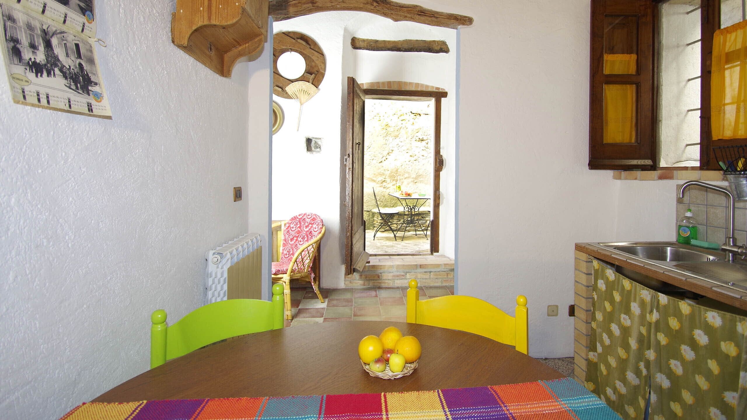 A cozy kitchen with a dining table, chairs, and a fruit basket.