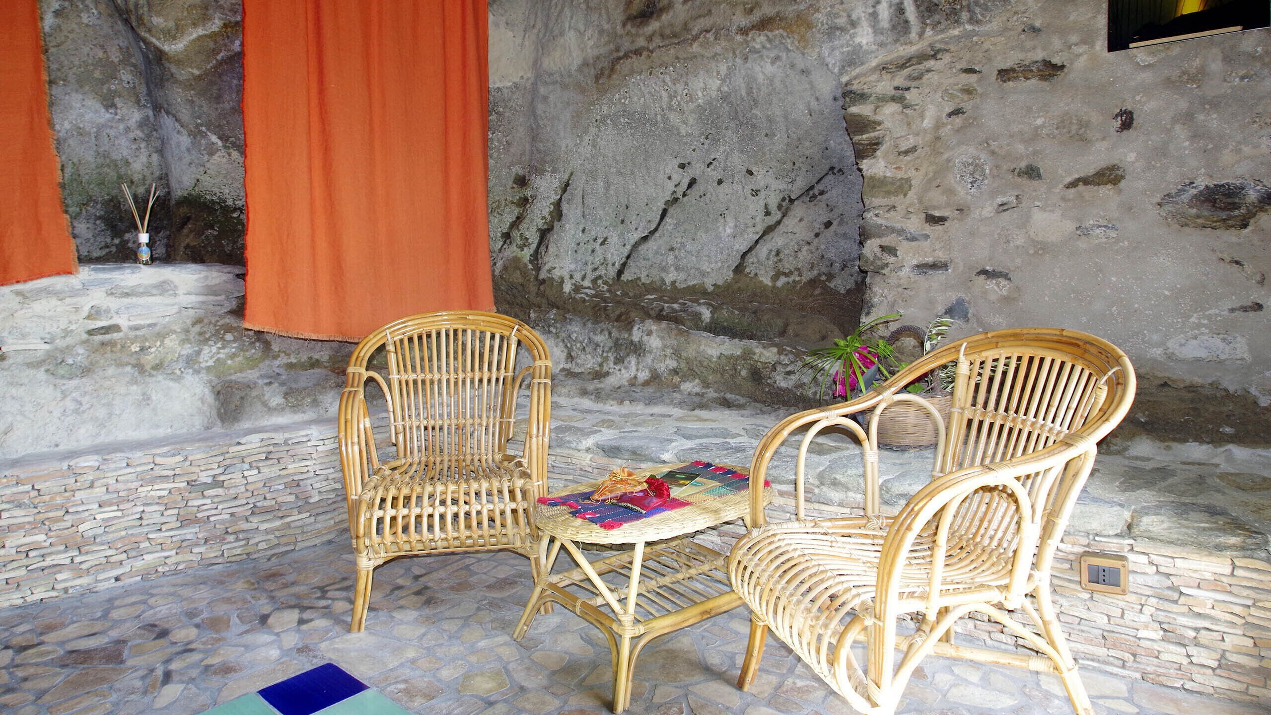 A stone-floored patio with two wicker chairs and a woven table.