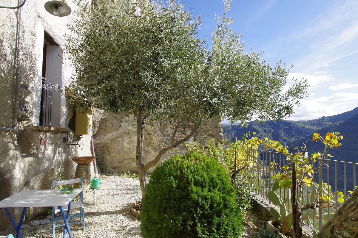 A rustic stone building with a small table and chairs outside, overlooking a mountainous landscape.