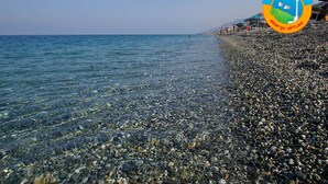 Una playa de guijarros con agua cristalina y un logo en la esquina.