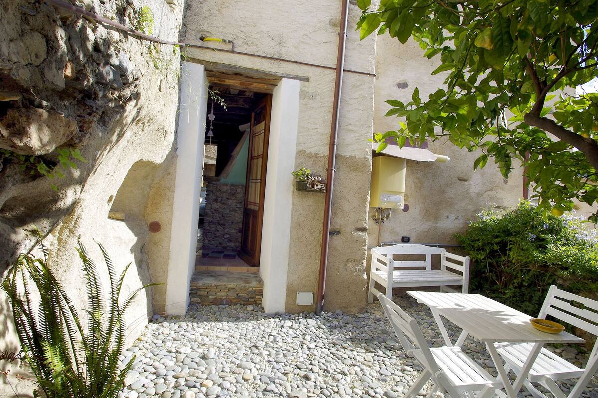 A rustic outdoor seating area with a stone wall, a wooden door, and a gravel path leading to a building.