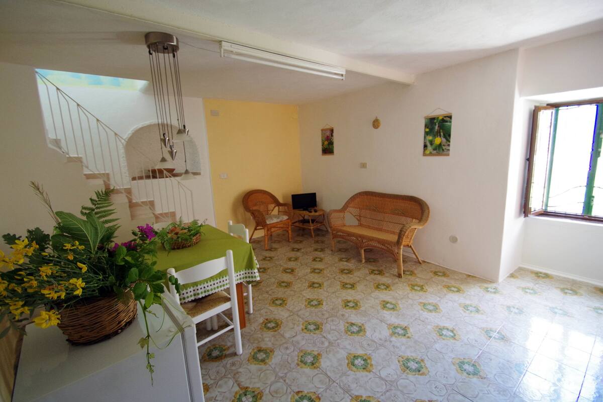 A dining area with a table set for two, a wicker sofa, and a small table with chairs.
