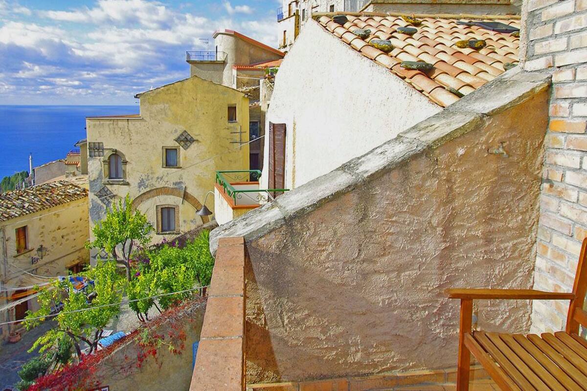 A narrow street with traditional buildings, a wooden bench, and a view of the sea.