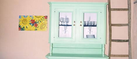A room with a light green cabinet, a blue patterned sofa, a ladder, and a painting of sunflowers.