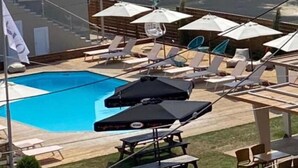 A pool area with lounge chairs and umbrellas, a wooden deck, and a view of the ocean. - Vicky's Guesthouse (Corfu)