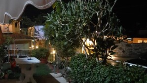 A nighttime view of a garden area with a small table and chairs, surrounded by greenery and a stone wall. - Vicky's Guesthouse (Corfu)