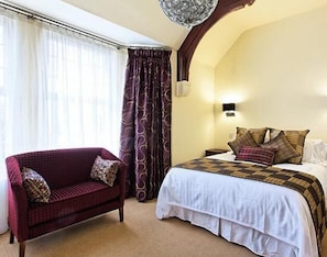 A hotel room with a bed, a red armchair, a nightstand, and a wall-mounted lamp. - Lucarelli Inn (West Bromwich)