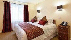 Een hotelkamer met een groot bed, een houten nachtkastje, een telefoon en een wandlamp.