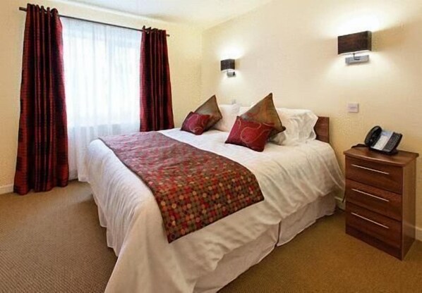 A hotel room with a large bed, a wooden nightstand, a telephone, and a wall-mounted light fixture.