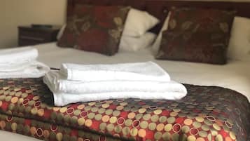 Un letto rifatto con cura, coperta a motivi, cuscini e asciugamani piegati.