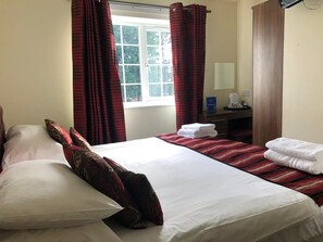 A hotel room with a large bed, two pillows, a bedside table with a lamp, and a window with curtains.