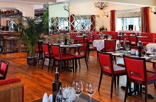 Um restaurante com assentos acolchoados em vermelho, mesas de madeira e um bar com garrafas de vinho.