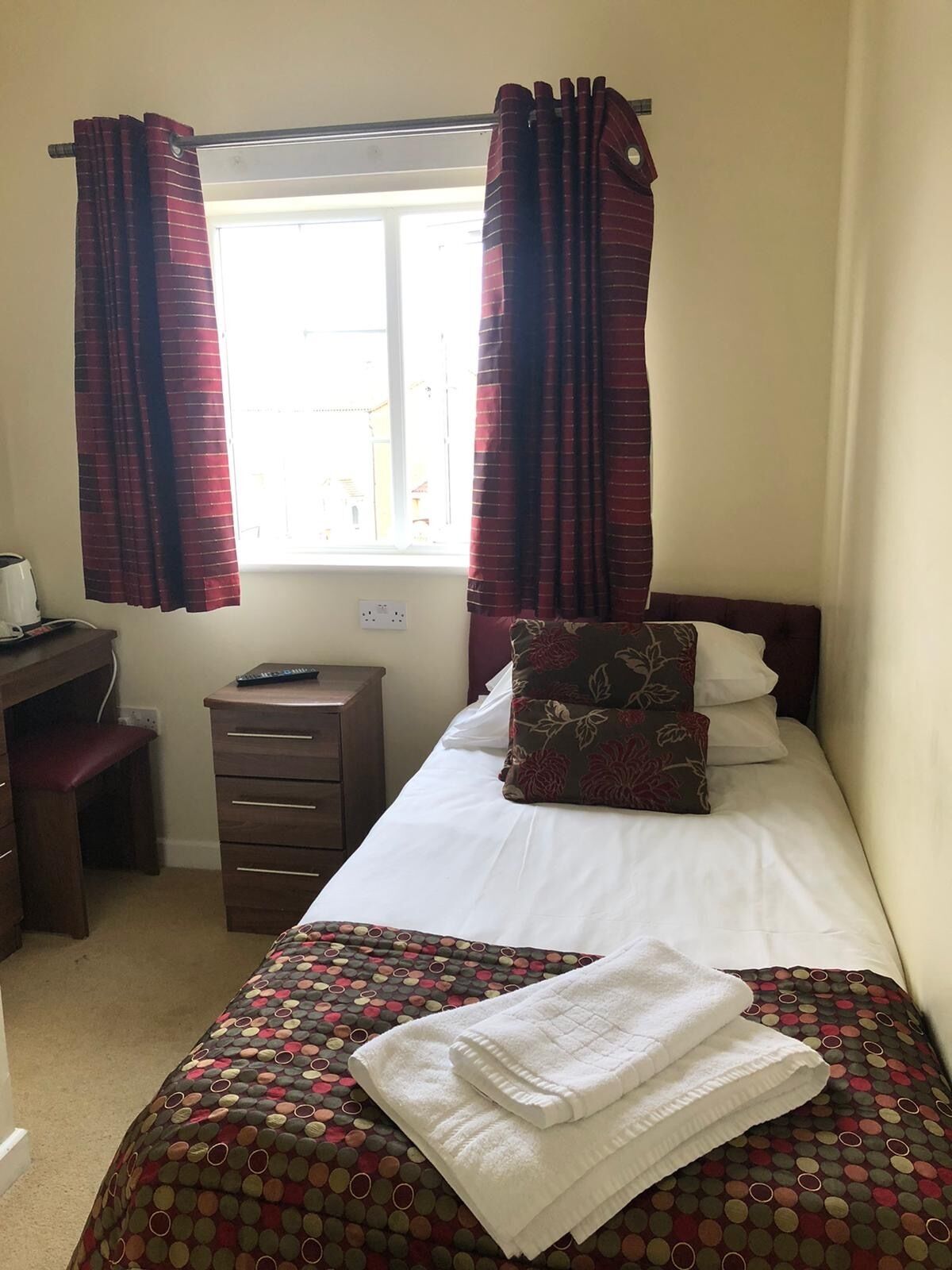 Un dormitorio con cama, escritorio y silla. Hay una ventana con cortinas.