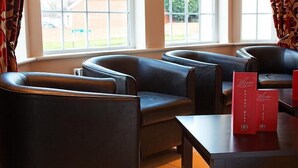 Een zithoek met lederen stoelen en een tafel, een raam met gordijnen, en rode menukaarthouders.