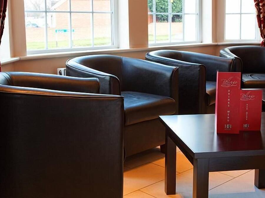 Un espace détente avec des fauteuils en cuir et une table, une fenêtre avec des rideaux et des présentoirs de menus rouges.