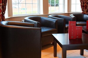 Uma área de estar com poltronas de couro e uma mesa, uma janela com cortinas e suportes de menu vermelhos.