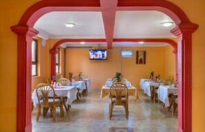 Un comedor con mesas y sillas, un televisor montado en la pared y un arco rojo.
