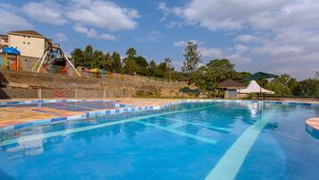 A swimming pool with a tiled deck, a slide, and a shaded area with a tent.