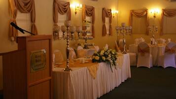 Un salón de banquetes con mesas dispuestas para un evento formal, con manteles blancos, centros de mesa florales y candelabros con velas.