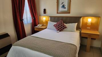 Ein Hotelzimmer mit einem großen Bett, zwei Nachttischen, einem Beistelltisch, einem gerahmten Bild an der Wand und roten Vorhängen.