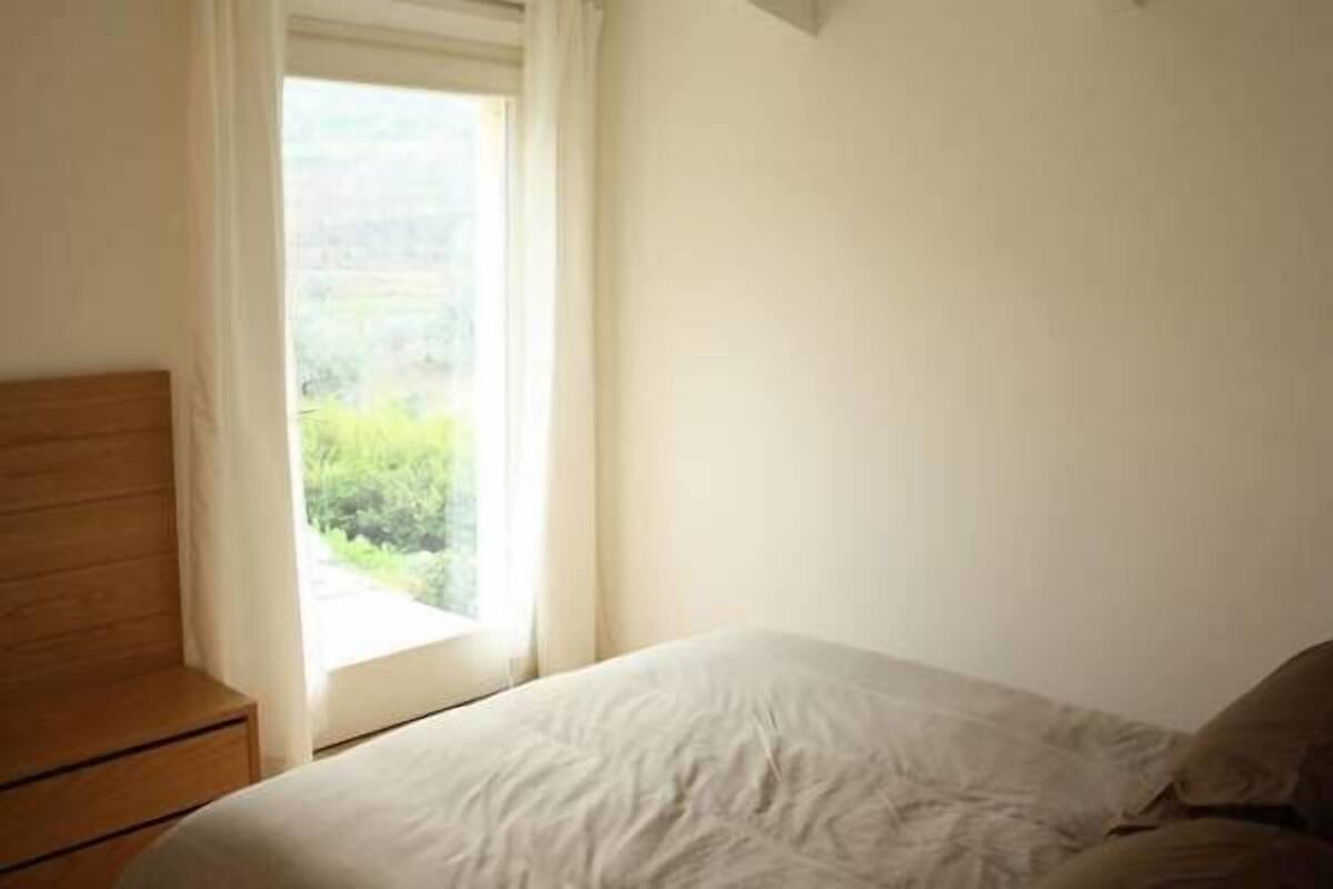 Une chambre à coucher avec un lit, une table de chevet en bois et une fenêtre donnant sur un paysage verdoyant.