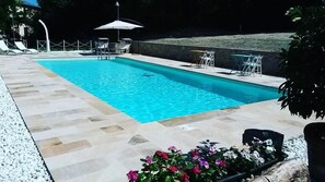 A rectangular swimming pool with a tiled deck, surrounded by lounge chairs and umbrellas. - Agriturismo La Barca nel Bosco (Fano)