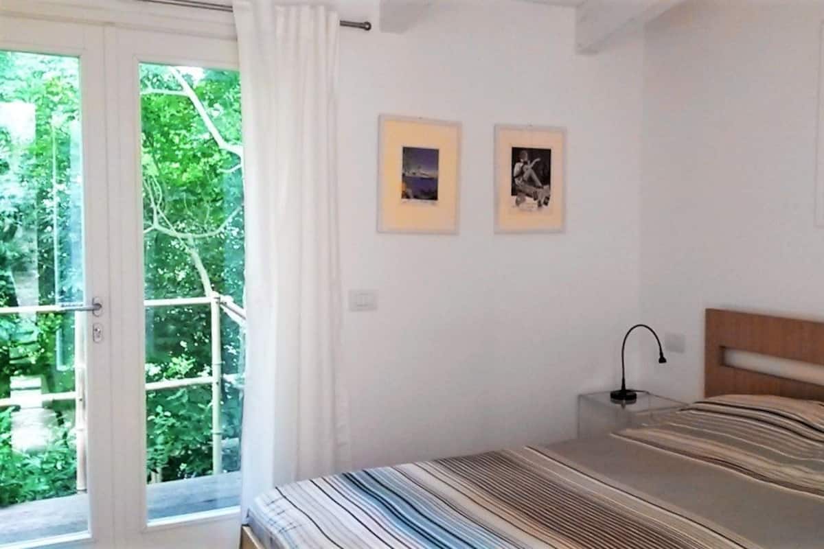 Une chambre à coucher avec un lit, une table de chevet, une fenêtre avec des rideaux et deux tableaux encadrés accrochés au mur.