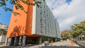 Ein modernes Gebäude mit einer markanten Fassade in Orange- und Grautönen, mit Balkonen und großen Fenstern.