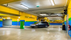 Eine mehrstöckige Parkgarage mit gelb-blauen Wänden, einem grünen Hinweisschild für den Ausgang und einem Feuerlöscher auf der rechten Seite.