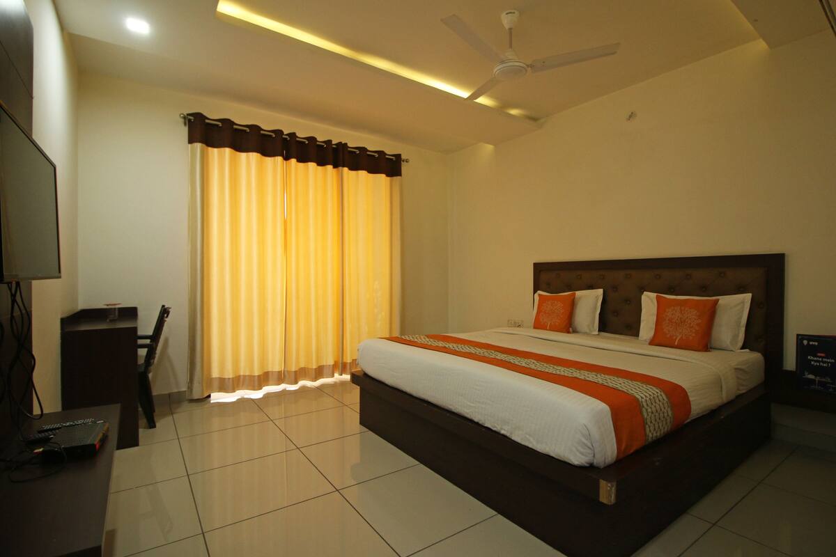 Une chambre d’hôtel avec un grand lit, un bureau avec une chaise, un ventilateur de plafond et des rideaux.