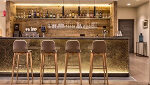 Una zona de bar con mostrador de madera, taburetes y una variedad de botellas y vasos.