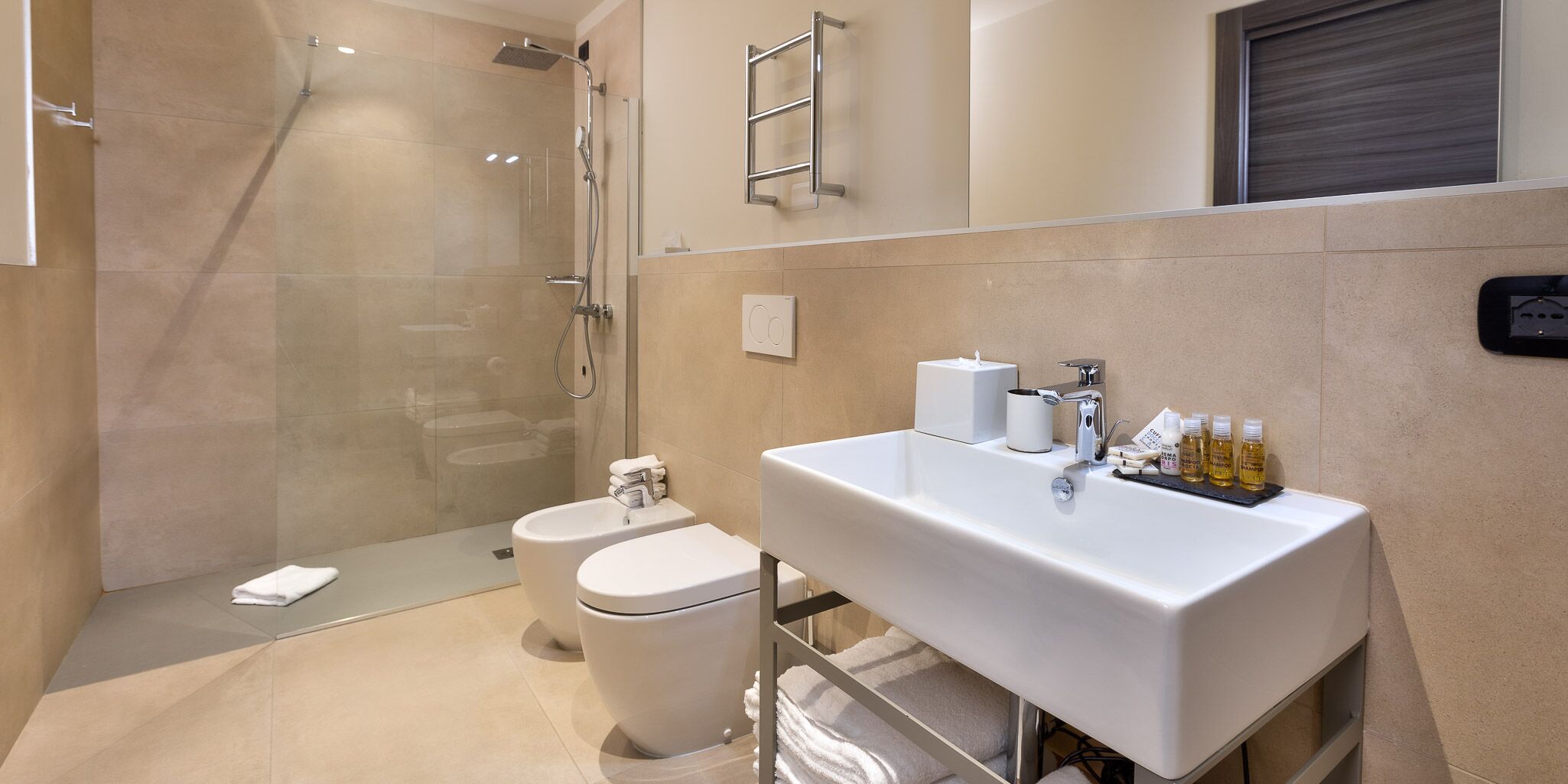 Une salle de bain moderne avec une douche à parois de verre, un lavabo blanc agrémenté d’articles de toilette et des toilettes.
