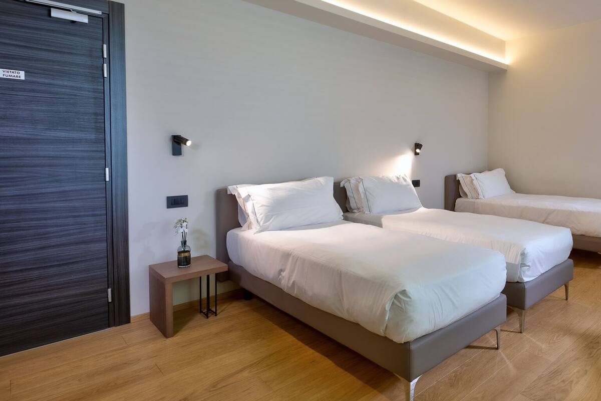 A modern hotel room with two beds, a small table with a vase, and a chair.