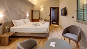 Una habitación de hotel moderna con una cama bien hecha, un área de descanso con una silla y una mesita, y un ventanal grande con persianas.