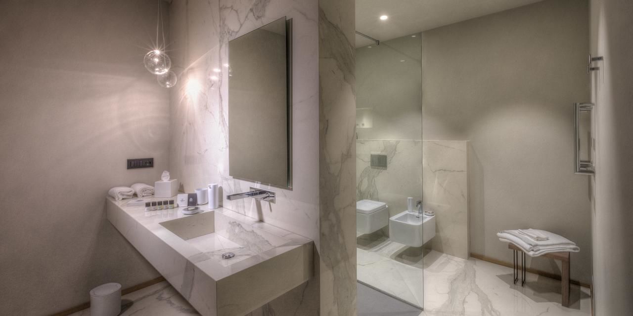 A modern bathroom with a large mirror, two sinks, a glass-enclosed shower, and a marble countertop.