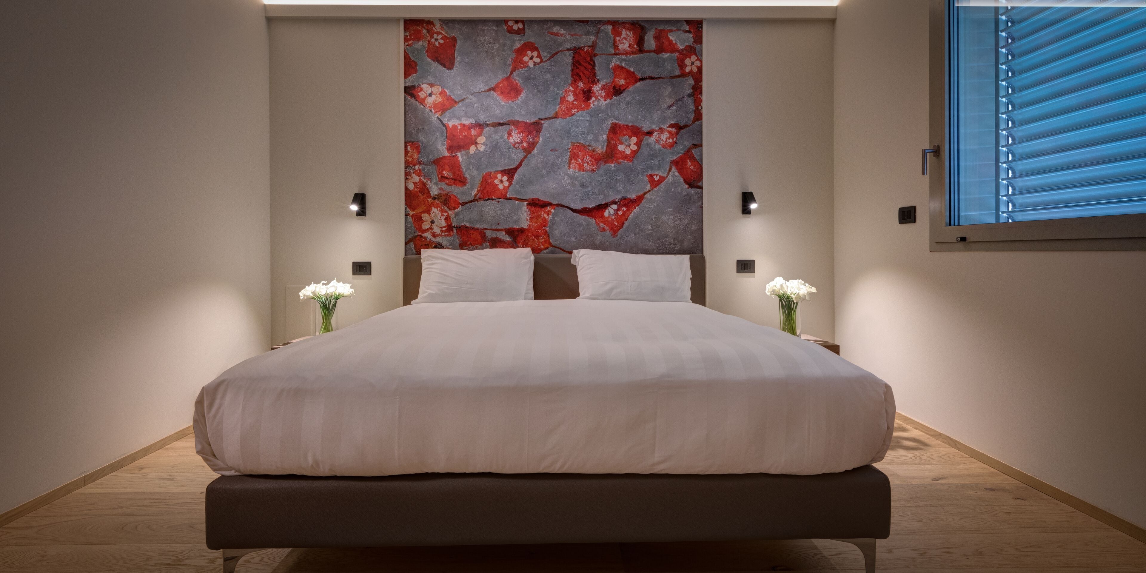 Quarto moderno com cama grande, parede decorativa e janela com persianas.