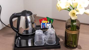 A coffee maker, two glasses, a vase with flowers, and some packaged food on a tray.